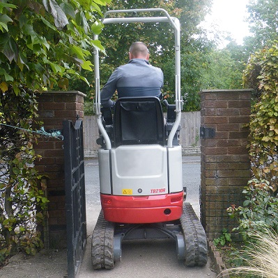 Takeuchi TB210R compact excavator passing through a garden gate